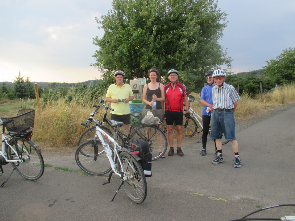 Gruppe von f&uuml;nf Radfahrern in Freizeitkleidung und Helmen, stehend neben ihren Fahrr&auml;dern auf einem Landweg.
