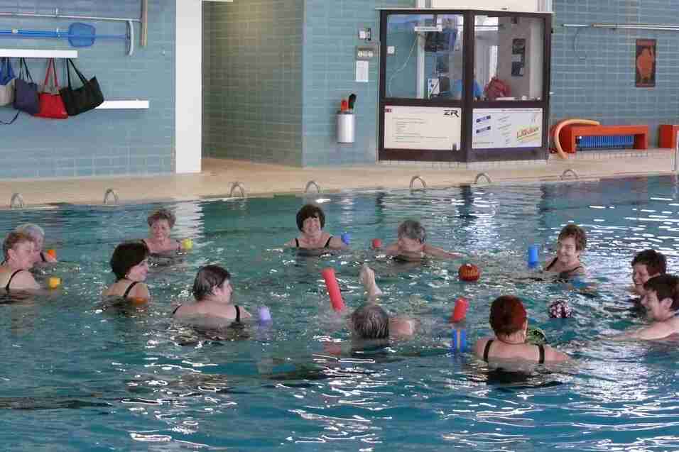 Gruppentraining im Wasser: Frauen mit Schwimmnudeln und Bällen stehen in einem Schwimmbecken.
