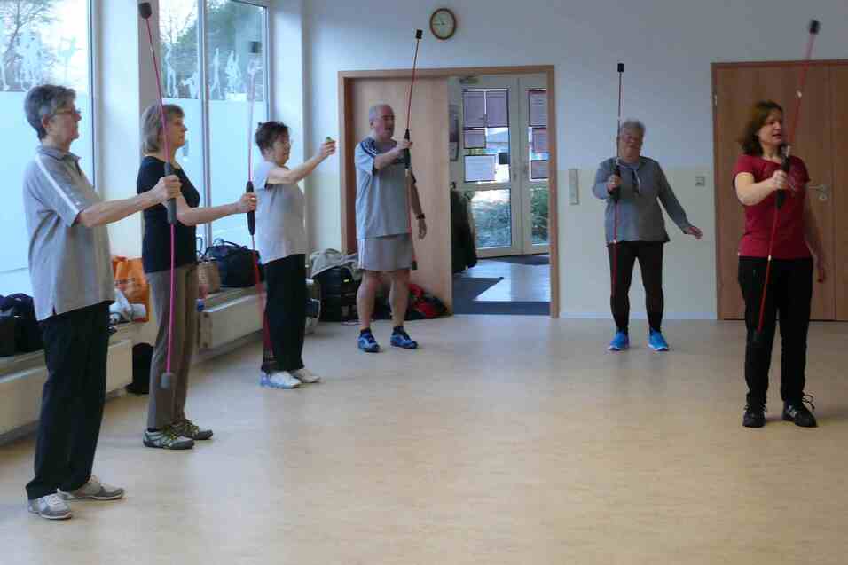 Gruppe von fünf Personen in Sportswear, die mit Stäben in einem Übungsraum trainieren.