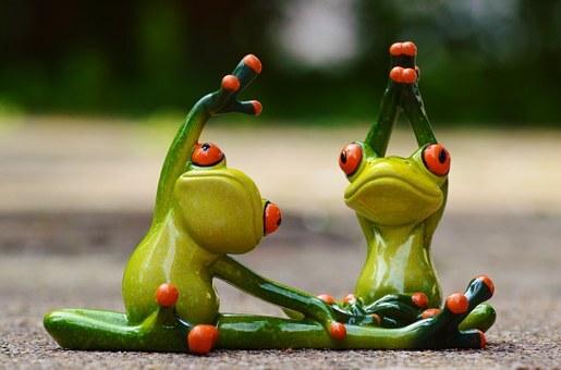 Zwei dekorative grüne Frösche in Yoga-Posen auf einer grauen Oberfläche, mit orangefarbenen Augen und Details.