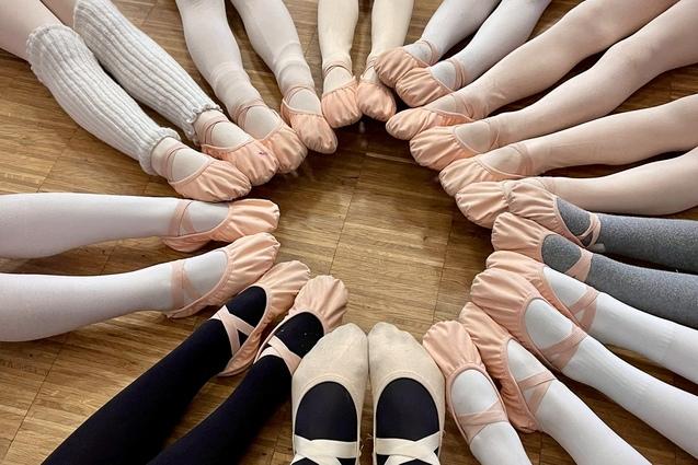 Kreis aus Tanzenden mit verschiedenen Ballettschuhen und Strumpfhosen auf einem Holzfu&szlig;boden.