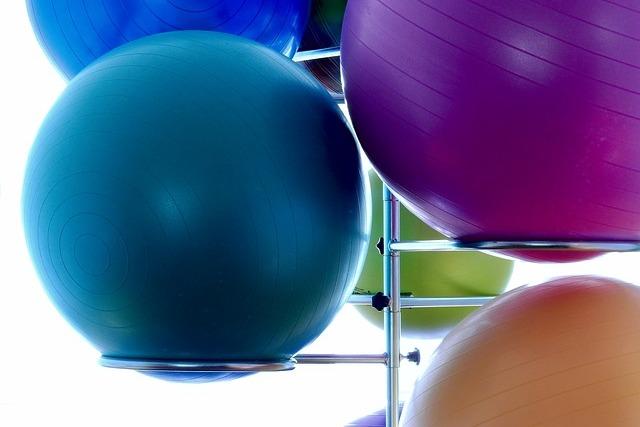 Bunte Fitnessb&auml;lle in verschiedenen Gr&ouml;&szlig;en h&auml;ngen an einem Gestell vor hellem Hintergrund.