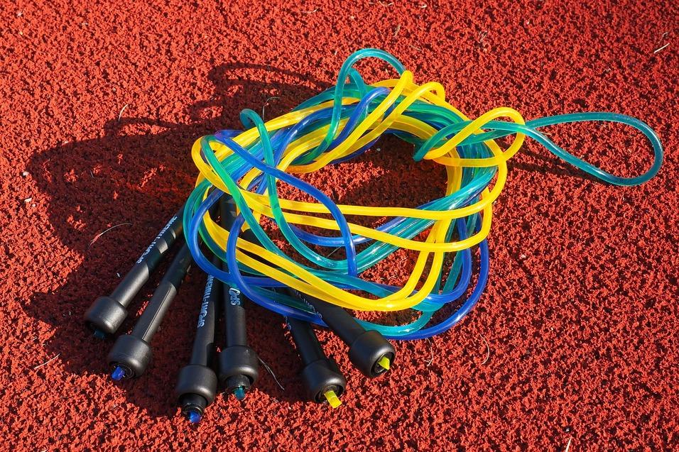 Bunte Springseile mit schwarzen Griffen liegen auf einer roten Sportplatzoberfl&auml;che.