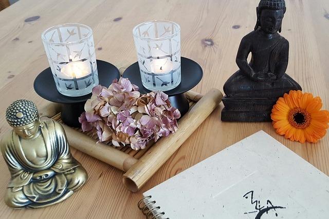 Dekoration aus Kerzenhaltern, einer Buddhafigur, Trockenblumen und einem Notizbuch auf einem Holztablett.