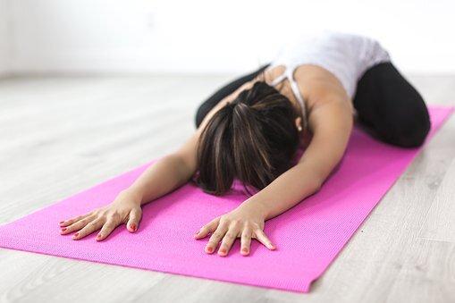 Frau in einer Yogaposition mit ausgestreckten Armen auf einer pinken Yogamatte im Raum.