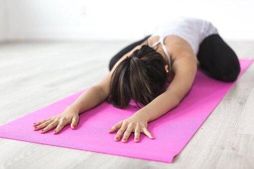 Frau in einer Yogaposition mit ausgestreckten Armen auf einer pinken Yogamatte im Raum.