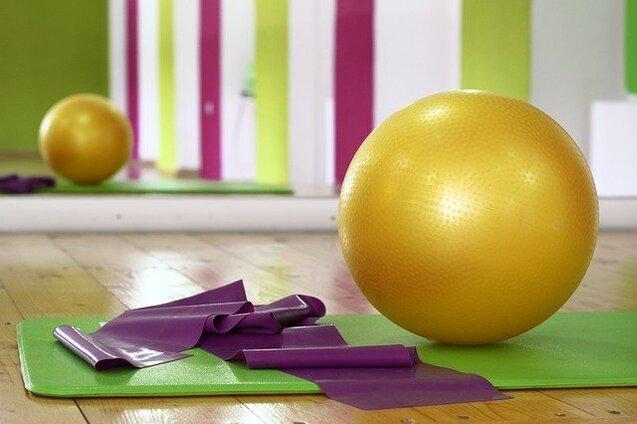 Goldener Gymnastikball und lila Widerstandsb&auml;nder auf einer gr&uuml;nen Trainingsmatte in einem Fitnessraum.