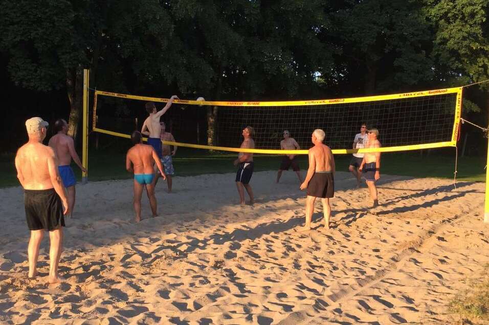 Gruppe von M&auml;nnern spielt Beachvolleyball auf einem Sandplatz unter Sonnenlicht.