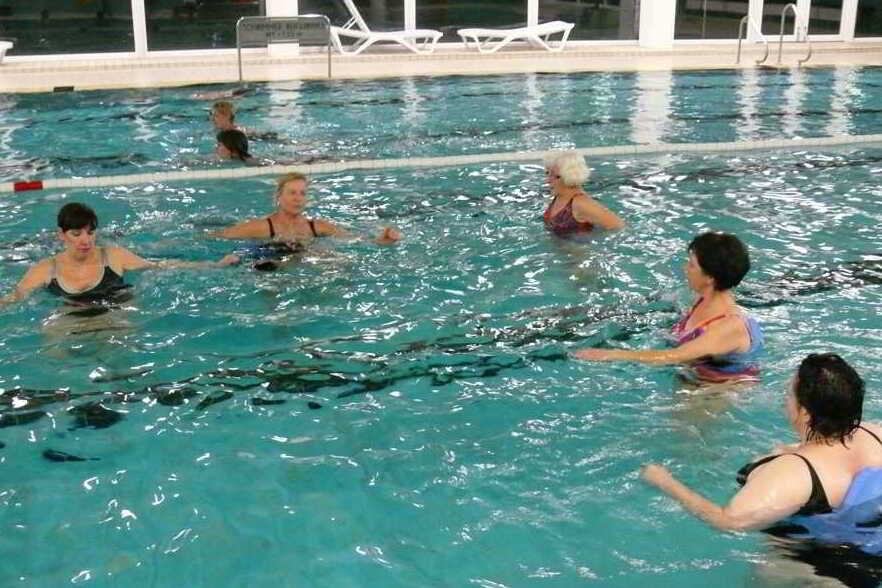 Gruppe von Frauen in Badebekleidung, die im Wasser eines Schwimmbades gemeinsam Wassergymnastik machen.
