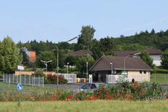 Landschaft mit einem Gebäude und Bäumen, umgeben von Gewächsen und einem Kreisverkehr mit Blumen.