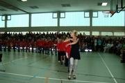 Tanzende Kinder in roten T-Shirts vor Publikum in einer Sporthalle während einer Aufführung.