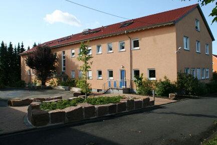 Einfamilienhaus mit Putzfassade, grünem Garten und angelegtem Weg, umgeben von Bäumen und Sträuchern.