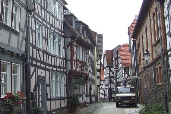 Engpass mit Fachwerkhäusern und einem alten Wagen in einer ruhigen, gepflasterten Straße. Wolkenreicher Himmel im Hintergrund.