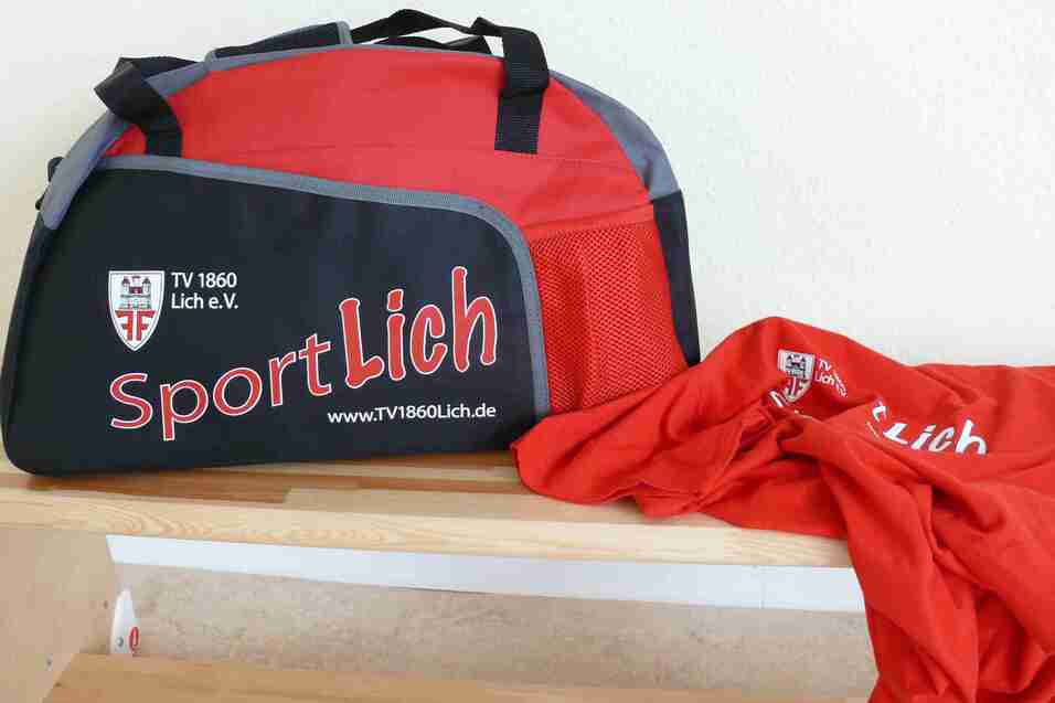Sporttasche in Rot und Schwarz mit Aufschrift "SportLich" und einem roten T-Shirt daneben auf einem Tisch.